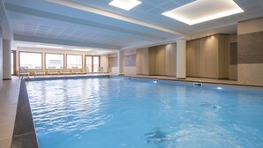 An indoor swimming pool with clear water, a tiled floor, and a seating area with chairs. - Résidence Club MMV l'Altaviva (Tignes)