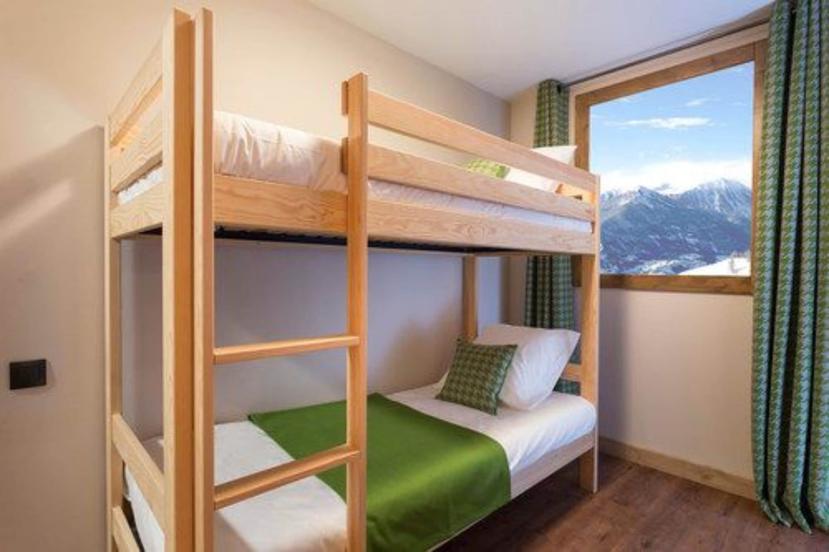 A bunk bed room with a mountain view, a window with curtains, and a green bedspread.