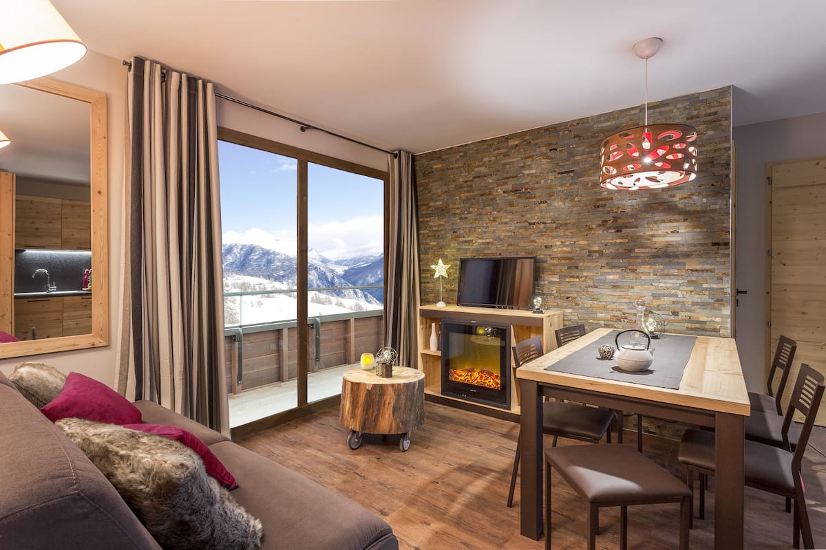 Una sala de estar moderna con chimenea, zona de comedor y un amplio ventanal con vistas a la montaña.