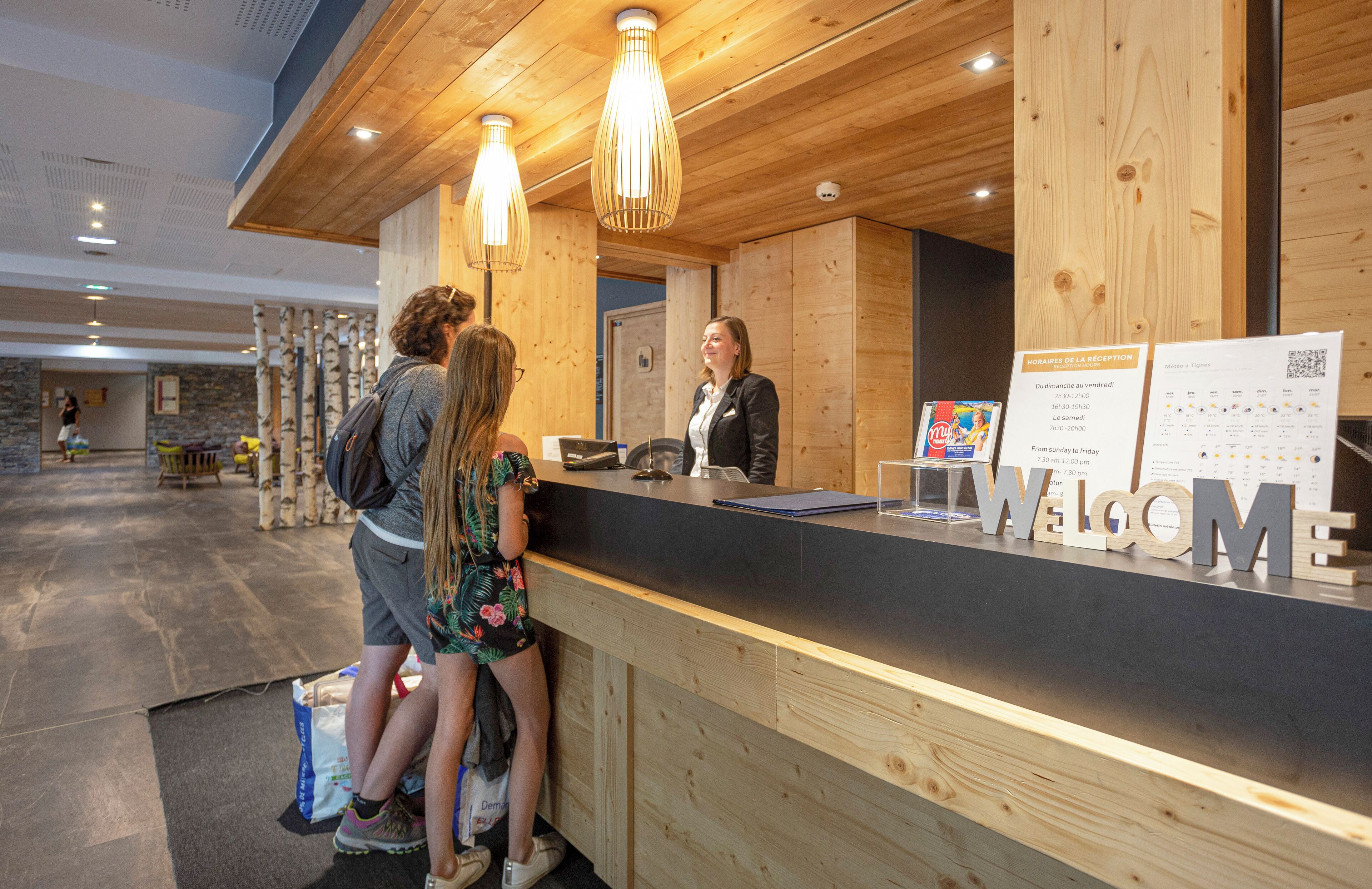 A reception desk with a "WELCOME" sign, wooden paneling, and hanging pendant lights.