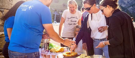 A group of people at an outdoor event with a table set with food and drinks.