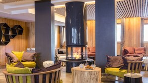 A modern interior with a central wood-burning stove, wooden panel walls, and cozy seating areas. - Résidence Club MMV l'Altaviva (Tignes)