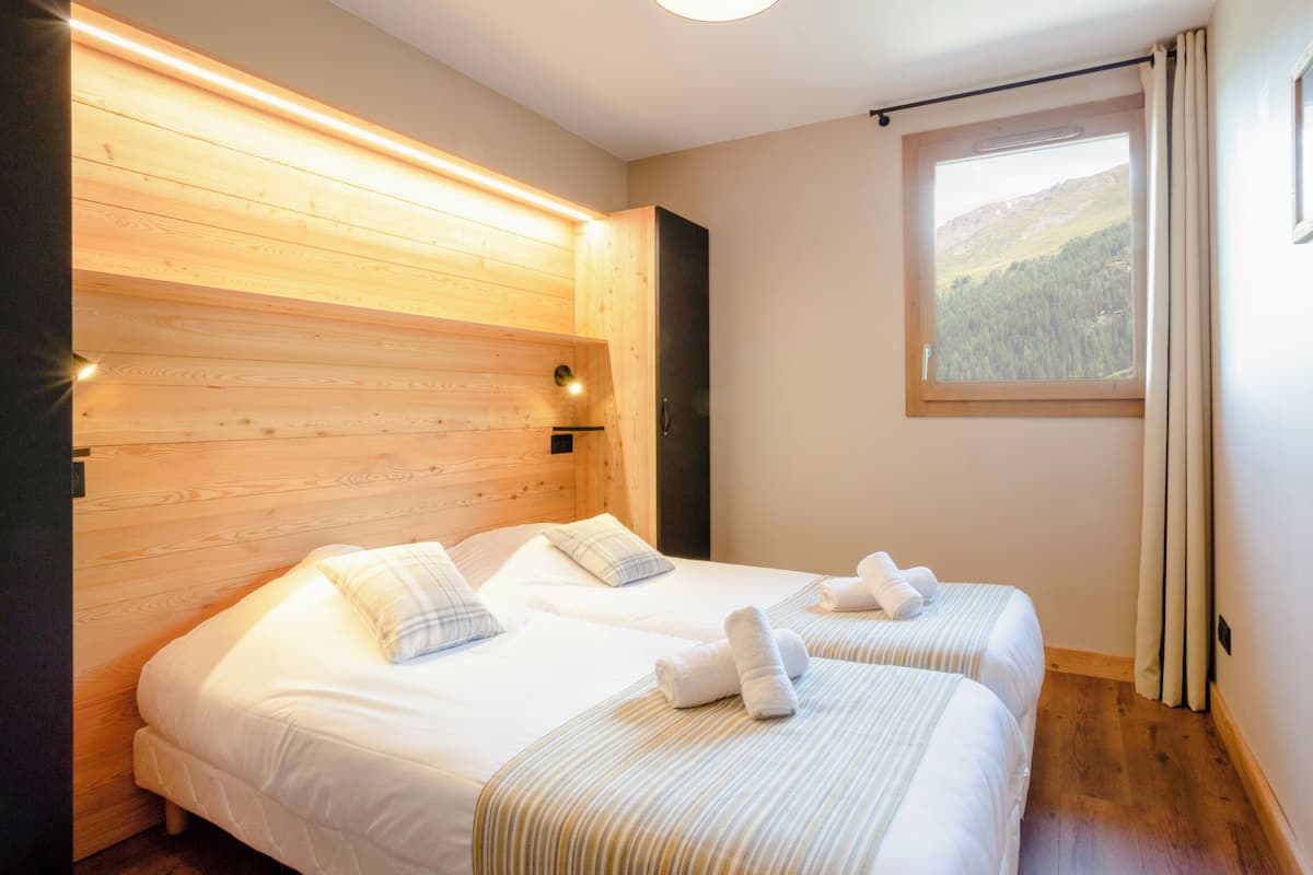 Una habitación con dos camas, cabecero de madera, una ventana con vistas a un bosque y una cortina.