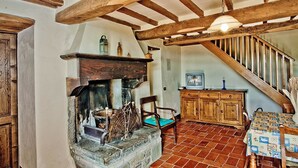 Un interior rústico con chimenea de piedra, vigas de madera, una escalera y un armario de madera.