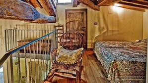 Una habitación rústica con una escalera de madera, una silla de mimbre, una cama con colcha estampada y una puerta de madera.