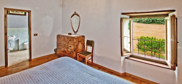 Un dormitorio con un aparador de madera, una silla, una cama grande, un espejo y una ventana con vista a un jardín.
