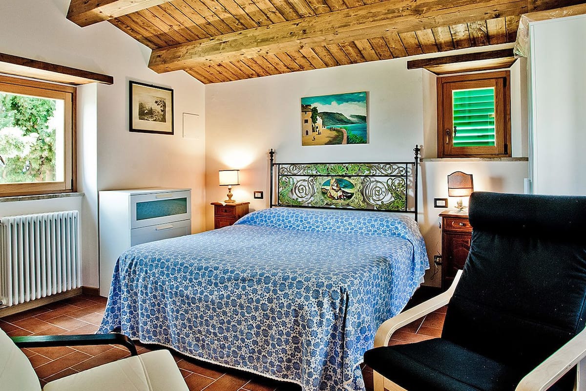 Ein Schlafzimmer mit einem Bett, zwei Stühlen, einem Heizkörper, einem Fenster und einem Bild an der Wand.