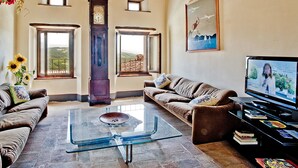 Una sala de estar con dos sofás, una mesa de centro de vidrio, un televisor y un ventanal con vistas al campo.