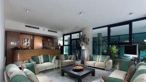 A modern hotel lobby with sofas arranged around a central coffee table, a reception desk, and large windows offering views. - Lido Hotel Residence (Cesenatico)