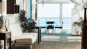 A modern living room with a white sofa, a coffee table, and a large potted plant. There is a balcony with a railing and a view of the sea. - Lido Hotel Residence (Cesenatico)