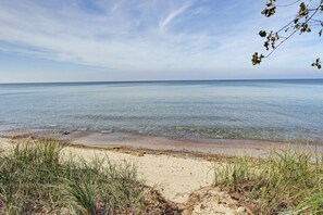 Una playa con aguas transparentes, orilla arenosa y vegetación escasa.