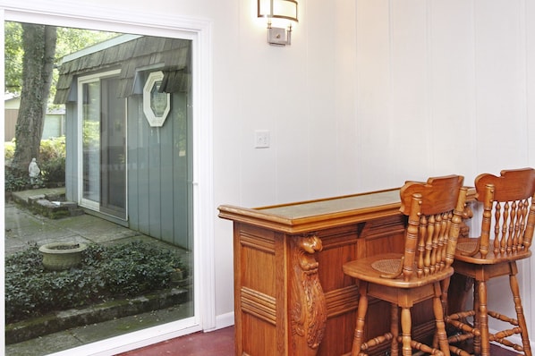 A wooden bar with two chairs, a glass door leading to a garden, and a wall-mounted light fixture.