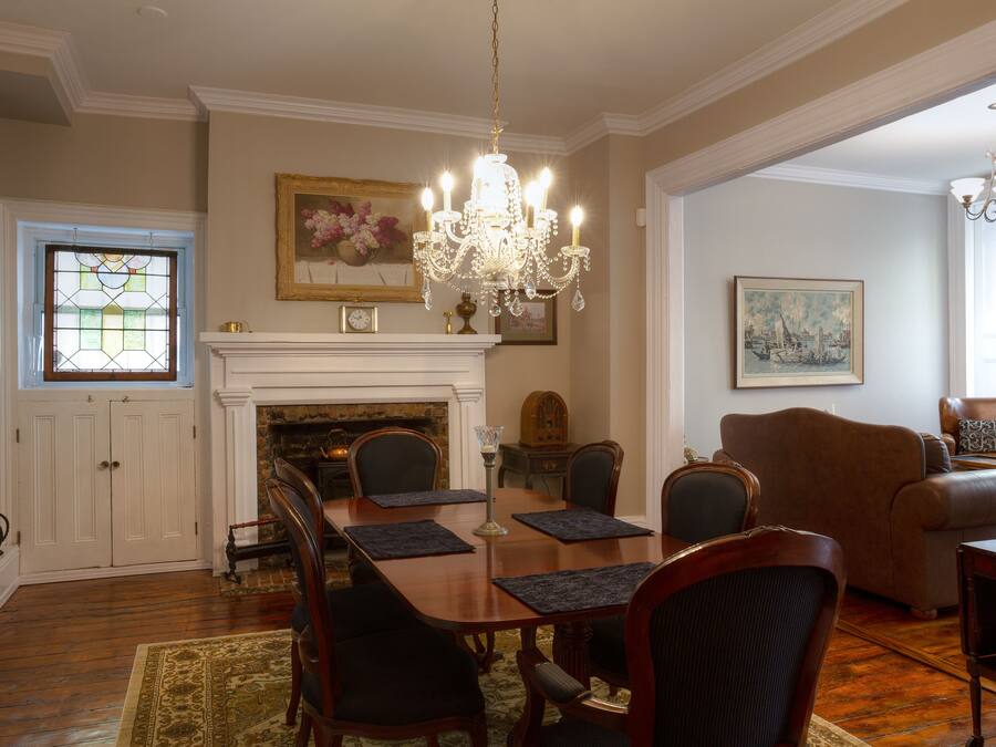 Un comedor con una mesa de madera, sillas, una araña, una chimenea y un cuadro en la pared.