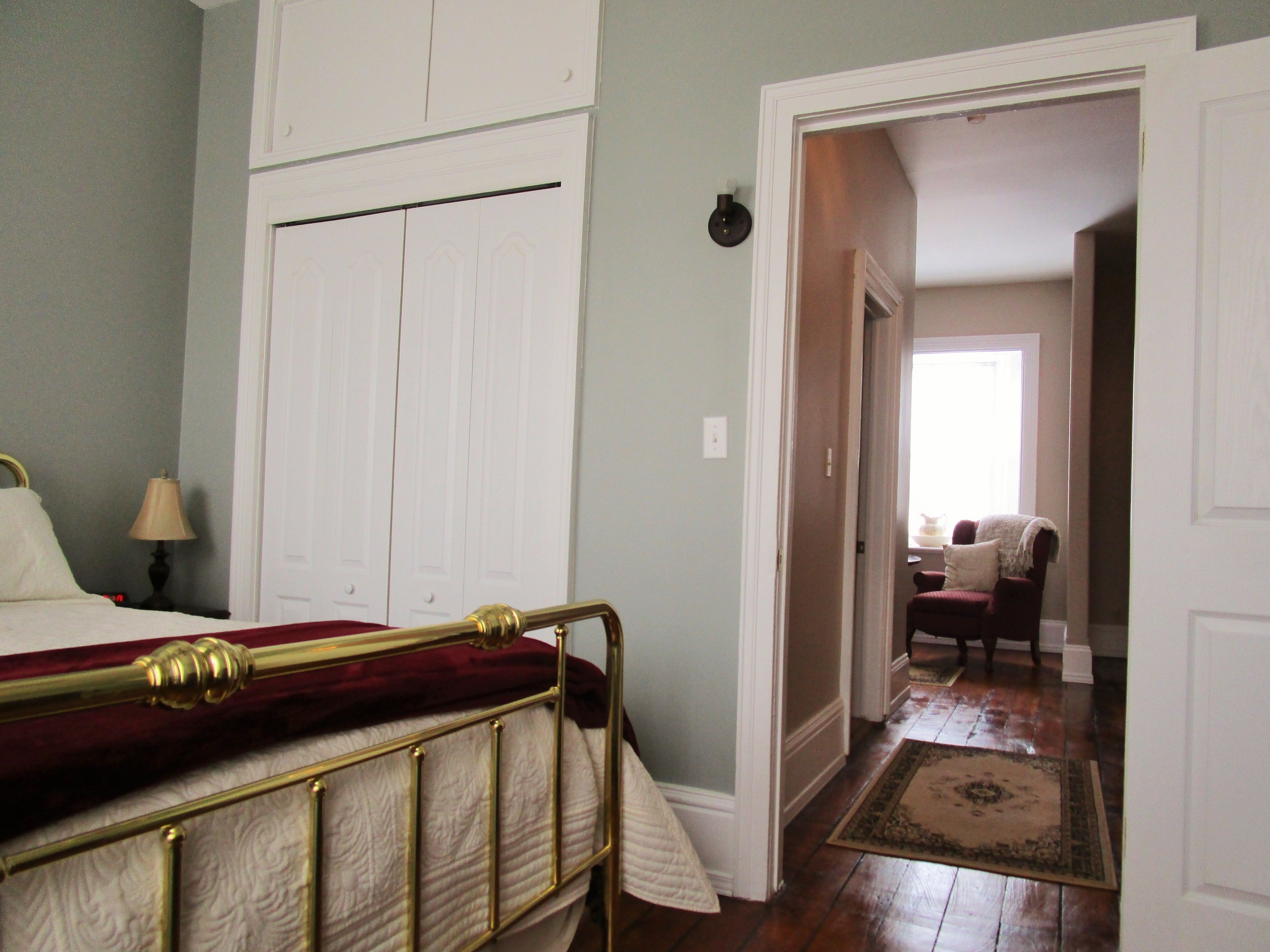 Un dormitorio con cama, mesita de noche, lámpara y una puerta que da a otra habitación.