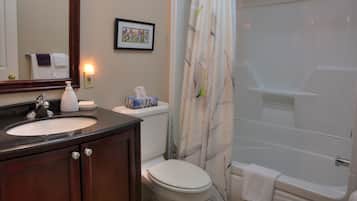 A bathroom with a sink, toilet, and bathtub. There is a framed picture on the wall, a towel rack, and a bottle of hand soap.