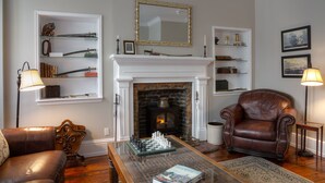 A living room with a fireplace, leather armchair, bookshelves, and a chessboard. - Sir Isaac Brock B&B Luxury Suites (Brockville)