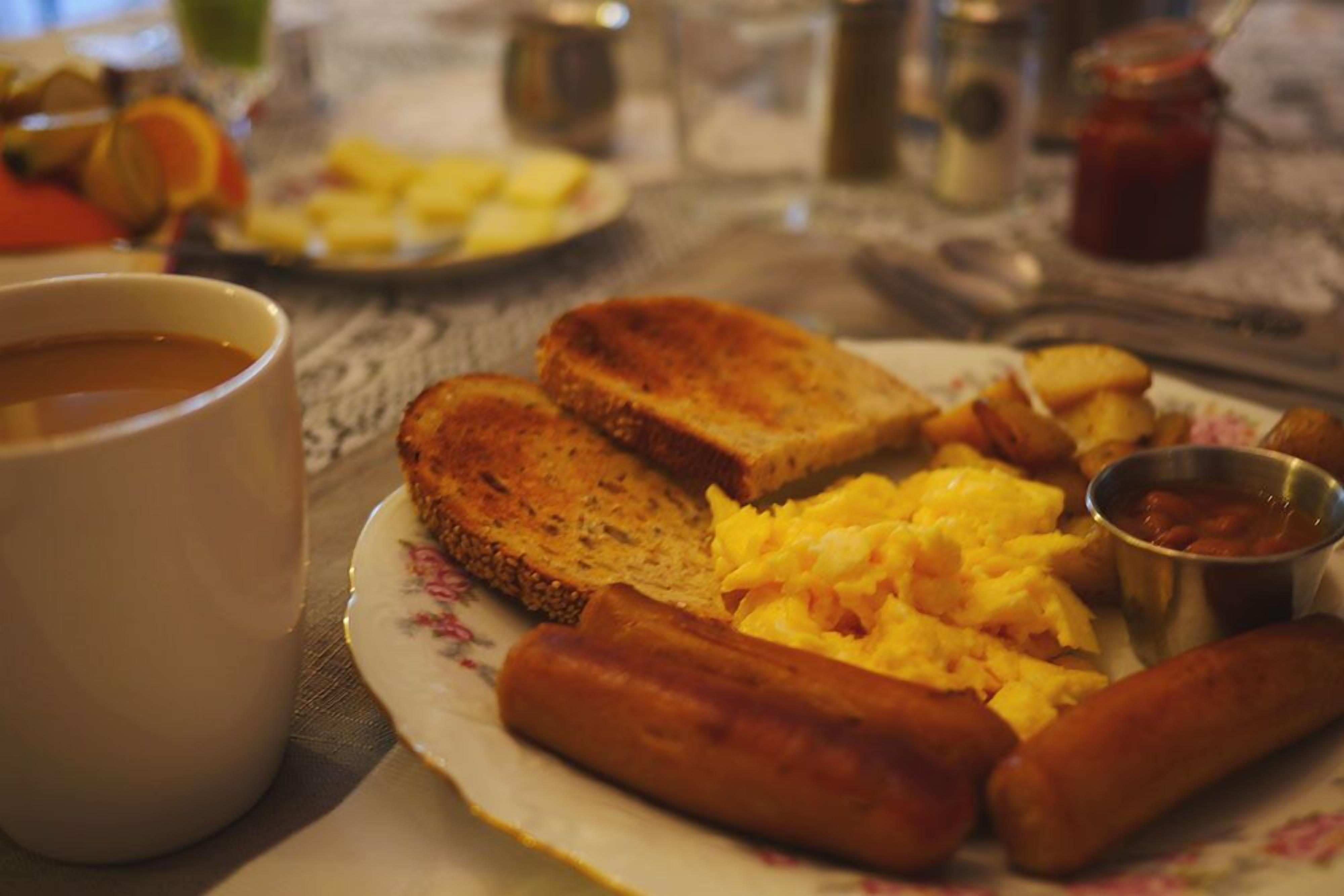 Un piatto da colazione con pane tostato, uova strapazzate, salsicce e una tazza di caffè.