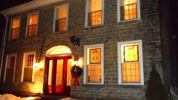 A stone building with multiple windows, a red door, and a snow-covered ground. - Sir Isaac Brock B&B Luxury Suites (Brockville)