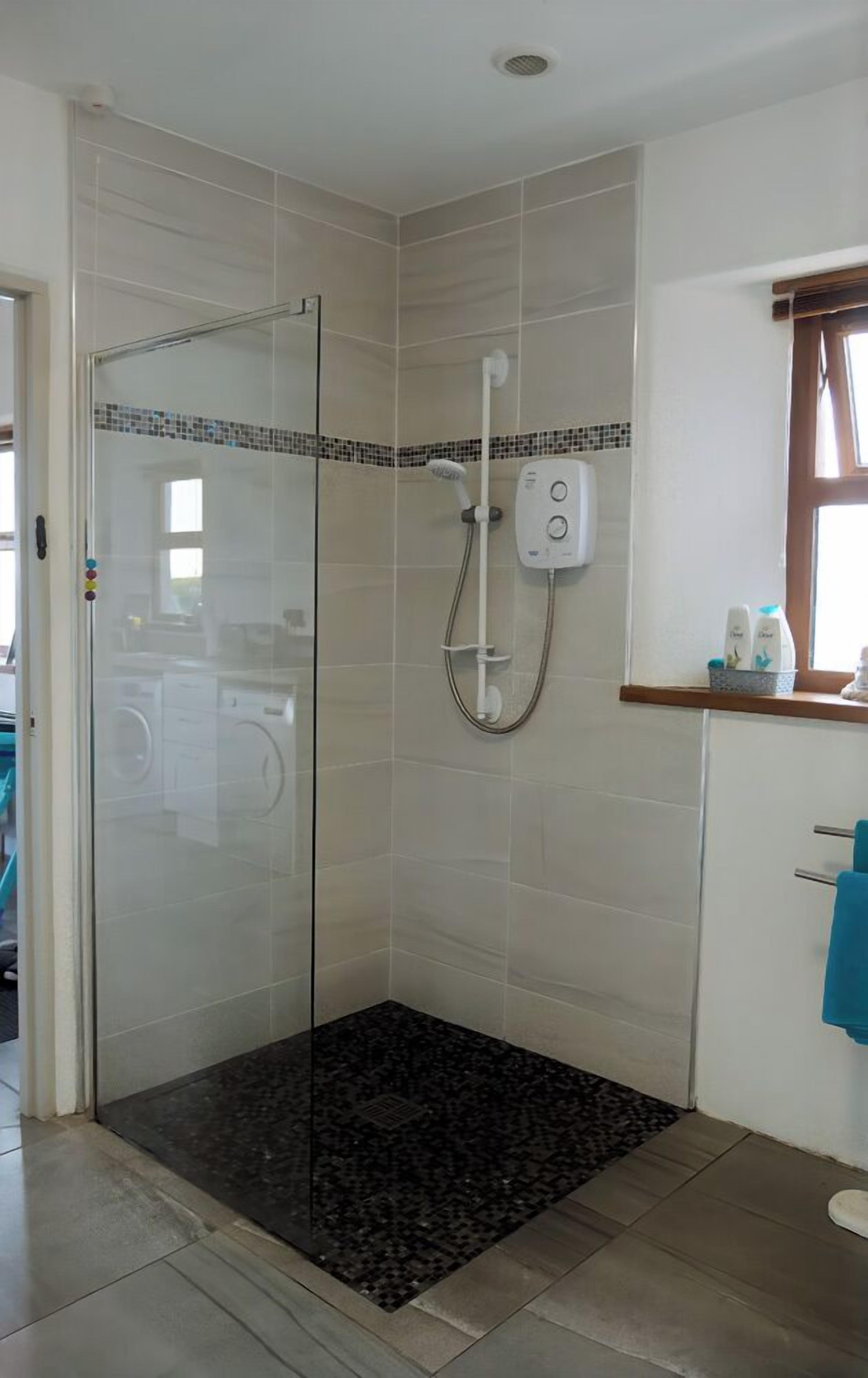 Ducha con puerta de vidrio, panel de control y un estante pequeño con artículos de aseo.