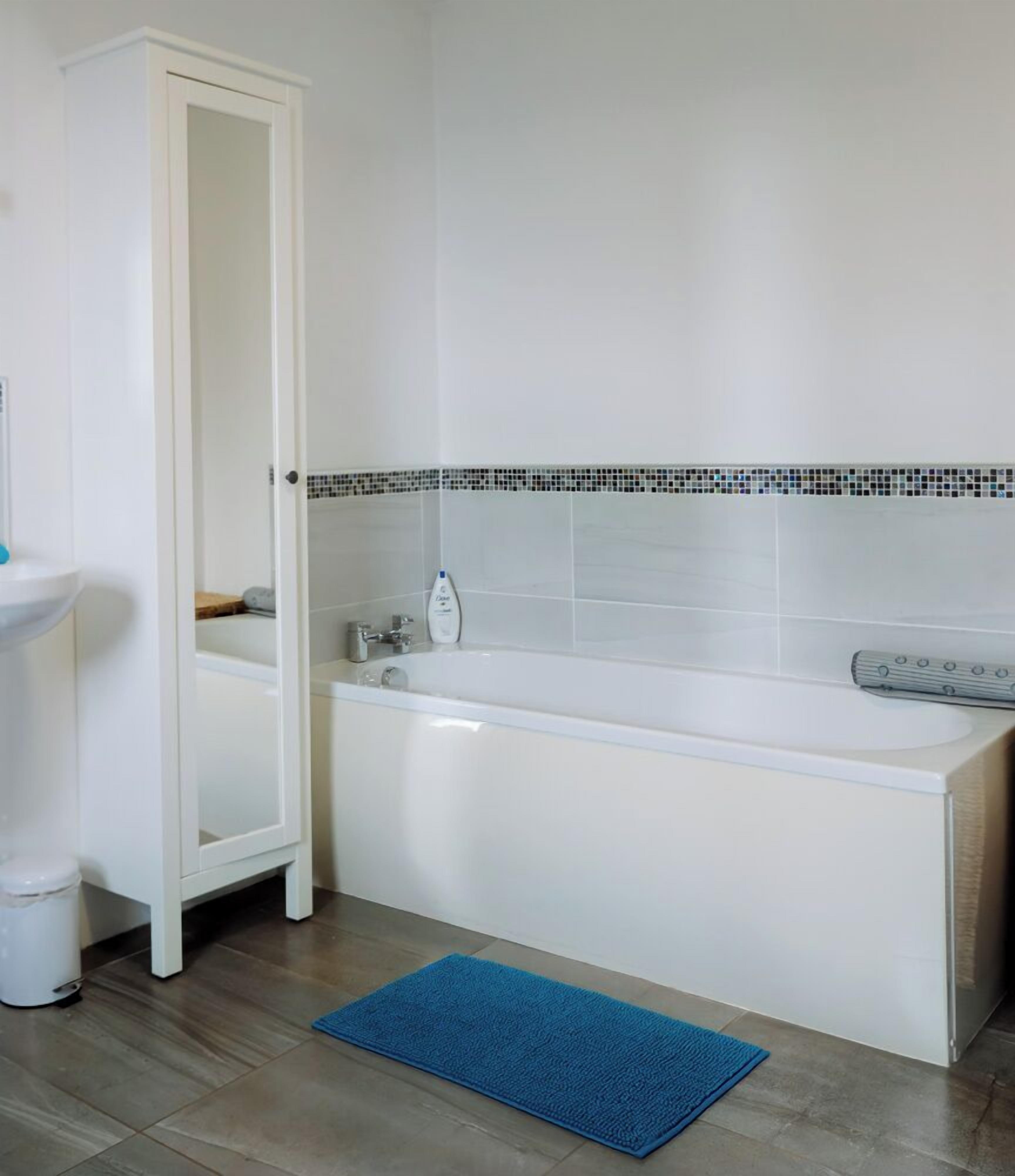 Un bagno con una vasca da bagno bianca, un tappeto blu, un lavandino bianco e uno schienale piastrellato.