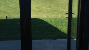 A room with a large sliding glass door leading to a grassy outdoor area with a view of the sea and distant mountains. - Kinbane Self-Catering (Ballycastle)