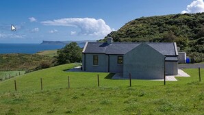 A house with a sloped roof, a small porch, and a view of the sea. - Kinbane Self-Catering (Ballycastle)