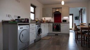 A compact kitchen with a washing machine, microwave, and oven. - Kinbane Self-Catering (Ballycastle)