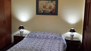 A bedroom with a bed, two bedside tables with lamps, a wall painting, and a wooden door. - Departamento Palma 75 (Parana)