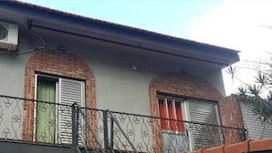 A building with two arched windows, a metal balcony railing, and an air conditioning unit mounted on the wall. - Departamento Palma 75 (Parana)