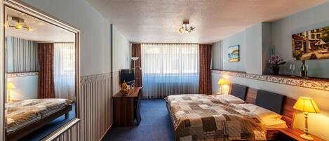Habitación de hotel con una cama grande, un escritorio, una silla, un espejo y una ventana con cortinas.