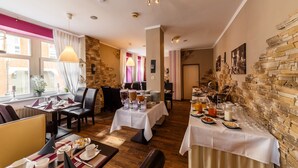 Uma sala de jantar com mesas preparadas para o café da manhã, com diversos pratos e bebidas.