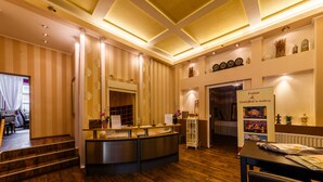 Área de recepção de hotel com chão de madeira, papel de parede listrado, balcão de recepção e exposição de atrações locais.