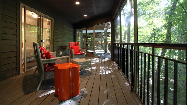 A wooden deck with wicker furniture and a railing overlooking a forest. - Treetops (Saugatuck)