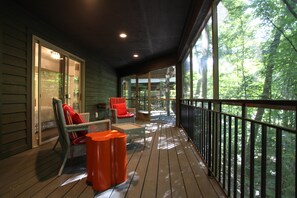 Une terrasse en bois, dotée de meubles en osier et d’une balustrade donnant sur une forêt.