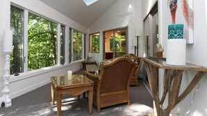 A spacious room with large windows, a wooden chair, a glass table, and a staircase with a railing. - Treetops (Saugatuck)