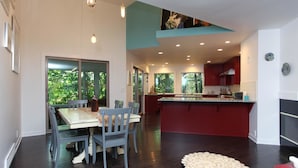 A modern kitchen with red cabinets, a central island, and a dining area with a table and chairs. - Treetops (Saugatuck)