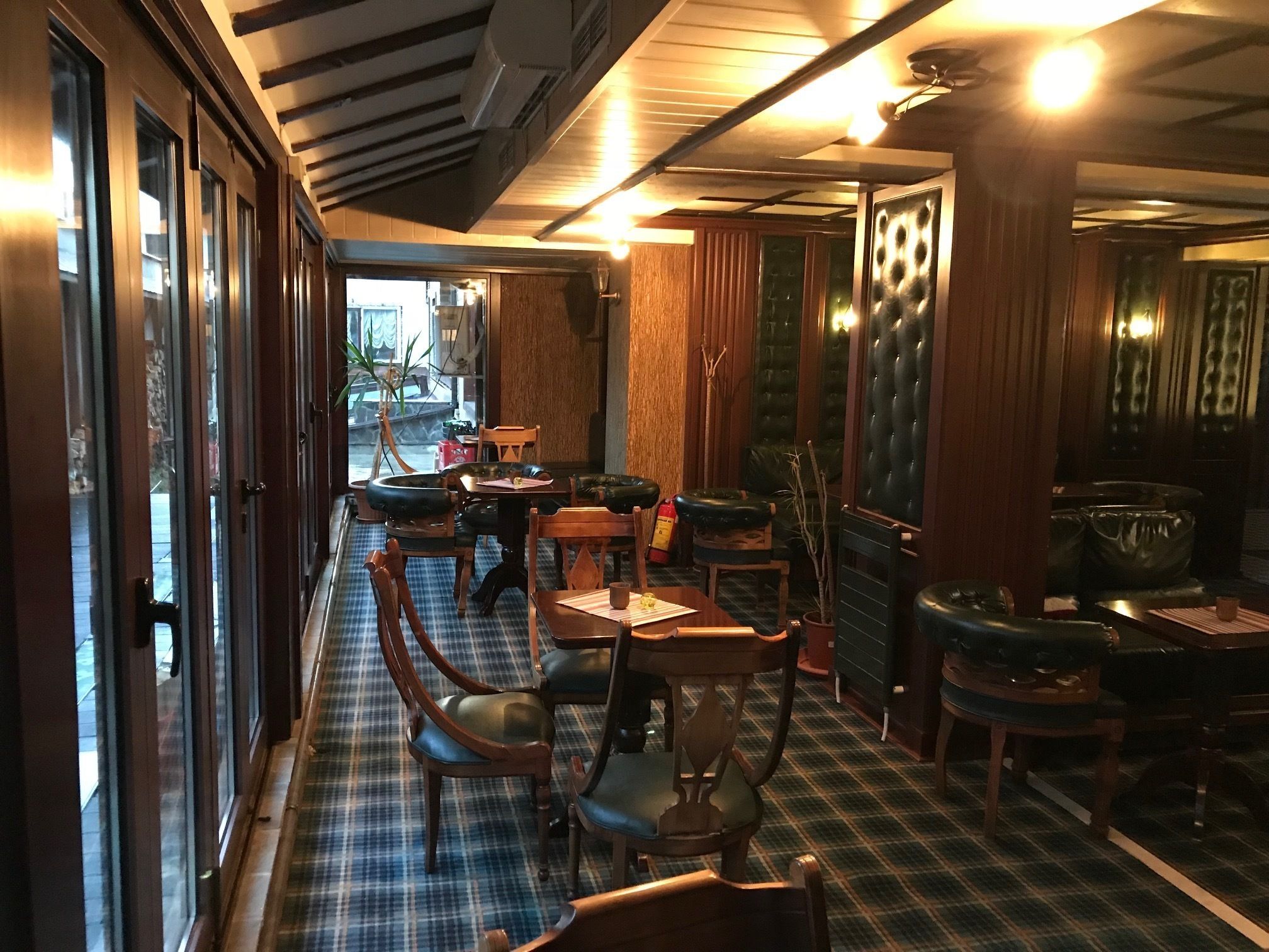A cozy restaurant with wooden furniture, plaid flooring, and a view through the open door.
