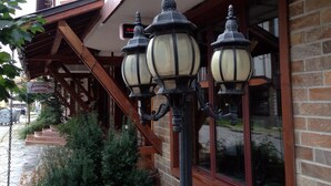 A brick building with a wooden staircase leading to a porch. There are three black street lamps on the porch. - Hotel Friends (Bansko)