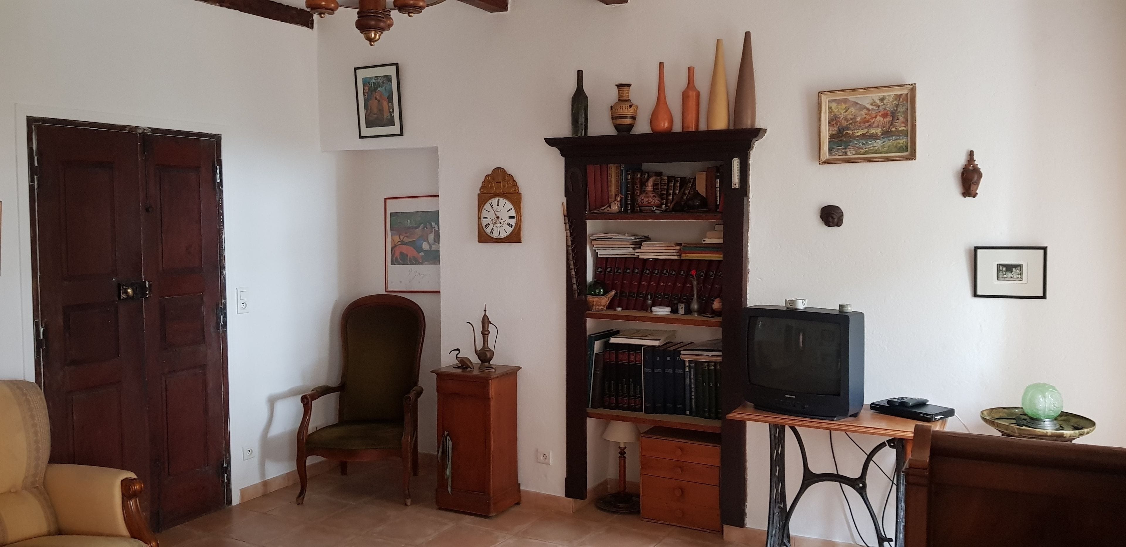 Una habitación con puerta de madera, un sillón verde, una estantería, un televisor y varios objetos decorativos.