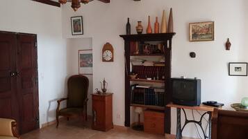 Una habitación con puerta de madera, un sillón verde, una estantería, un televisor y varios objetos decorativos.