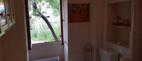 A bathroom with a toilet, sink, and a radiator. There is a window with a view of greenery outside.