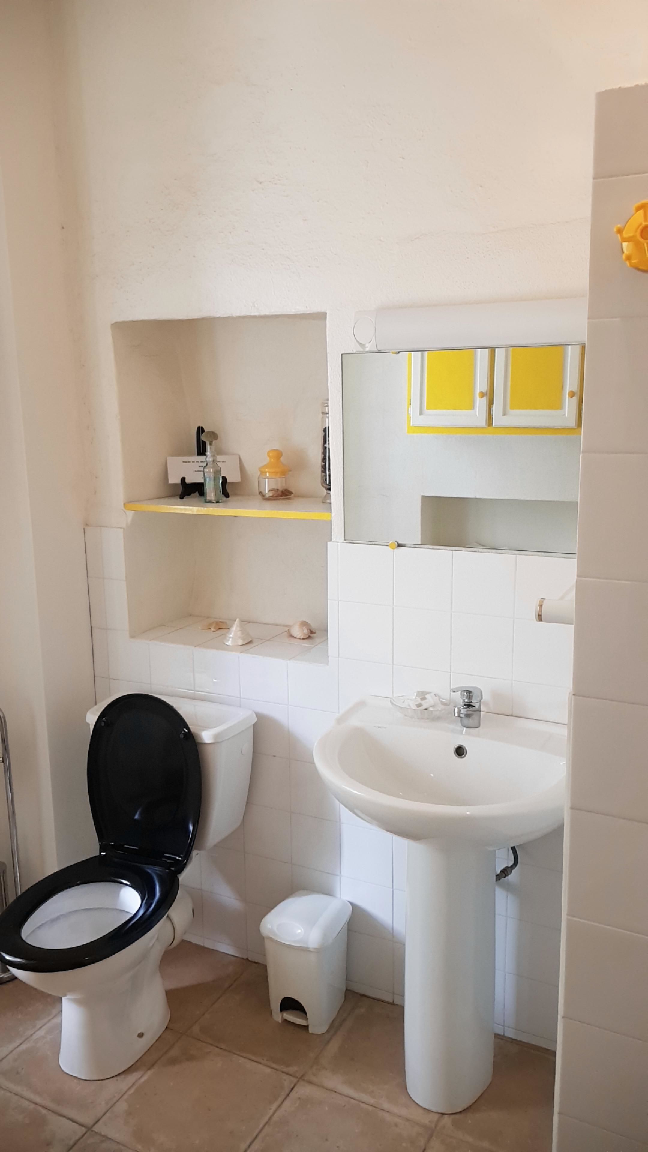 A small bathroom with a toilet, sink, and a shelf above the toilet.