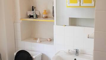 A small bathroom with a toilet, sink, and a shelf above the toilet.