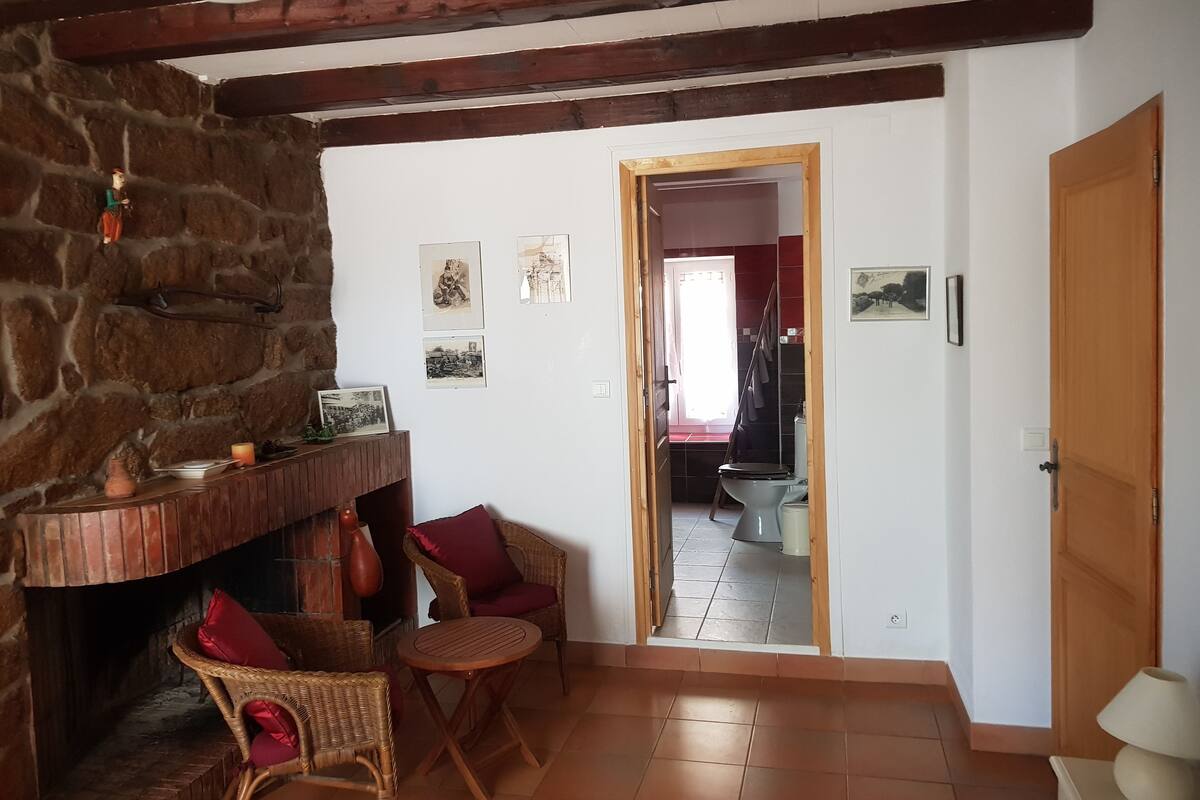 Una sala de estar acogedora con pared de piedra, chimenea, muebles de mimbre y suelo de baldosas.