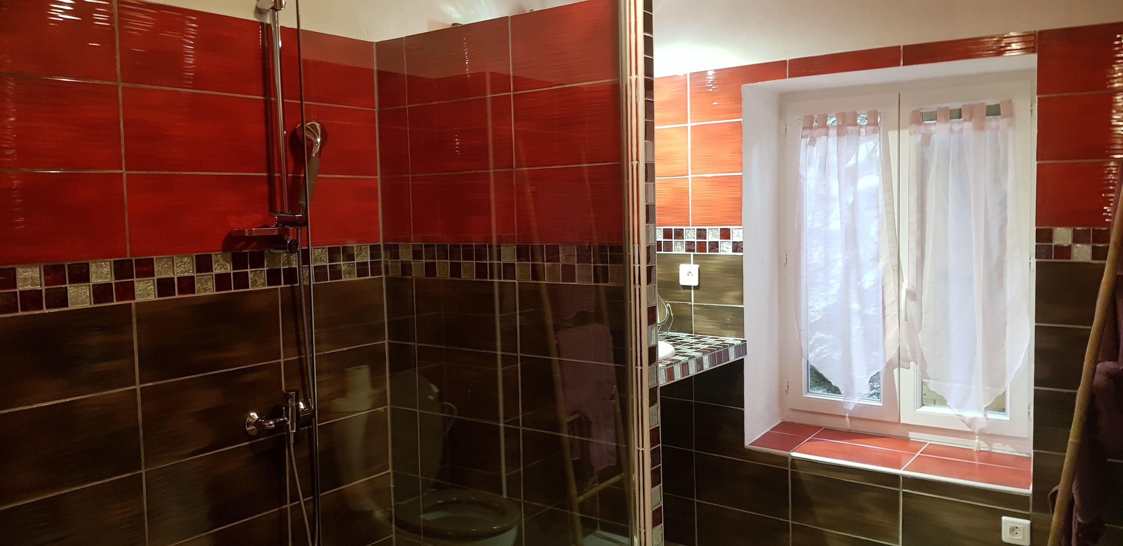 Un bagno con doccia vetrata, una finestra con tenda e pavimento piastrellato.