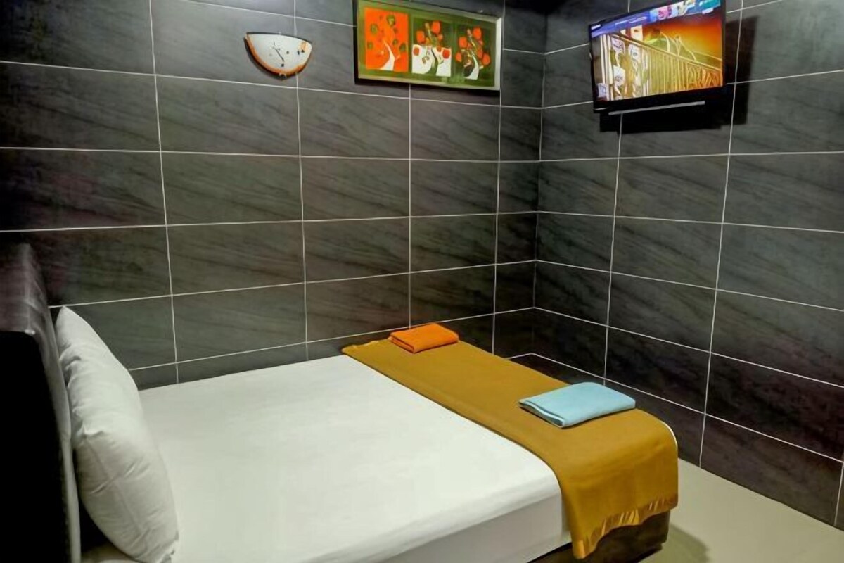 Una habitación pequeña con una cama, un televisor y un reloj de pared.