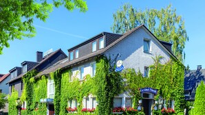 Un hotel con paredes cubiertas de hiedra, un cartel que dice 'Gruner Saud' y jardineras con flores.