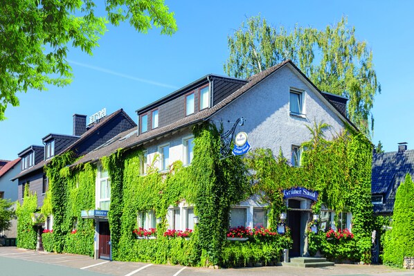 Un hotel con paredes cubiertas de hiedra, un cartel que dice 'Gruner Saud' y jardineras con flores.