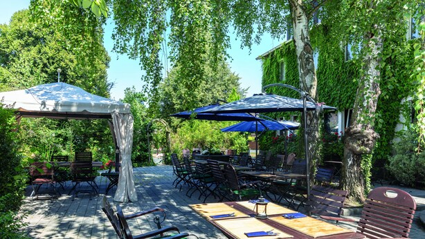 Un patio al aire libre con mesas y sillas, rodeado de follaje y árboles.