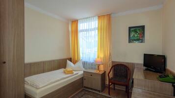 A hotel room with a bed, bedside table, lamp, chair, TV, and a painting on the wall.